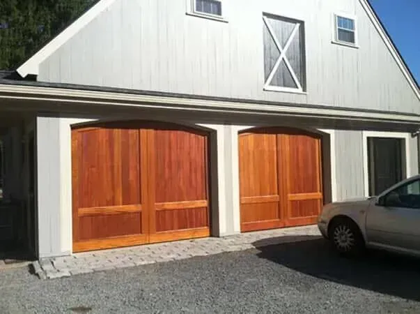 White garage with two wooden doors and a parked gray car on a gravel driveway