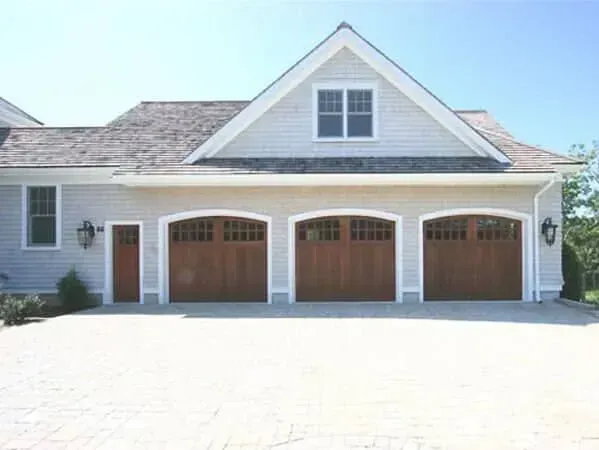 House exterior with three wooden garage doors and a white gabled dormer above a bright driveway