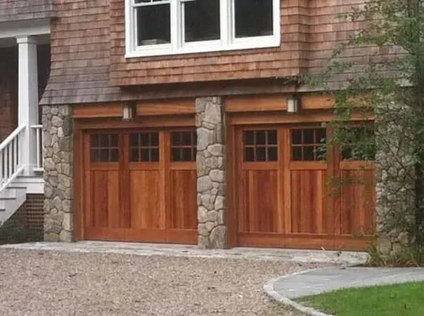 Two wooden garage doors beneath a house with shingle siding and white-framed windows