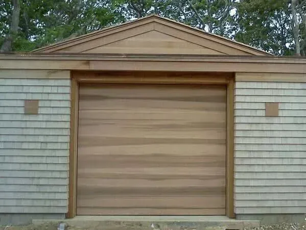 Wooden garage door on a small shed with tan shingles and a triangular roof
