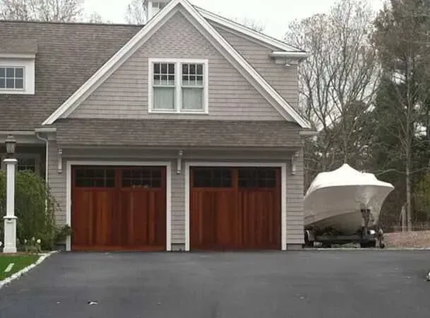 Gray house with two red garage doors and a boat parked in the driveway
