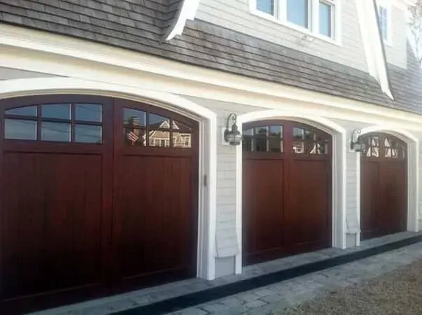 Three dark wood garage doors with white trim on a house exterior