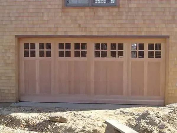 Wooden garage door with small window panes set in a brick wall above a dirt foreground.