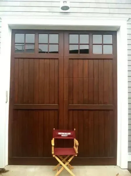 Large brown wooden double doors with small windows, fronted by a folded red chair on a white building exterior