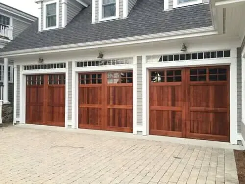 Three wooden garage doors on a gray house with white trim and paved driveway