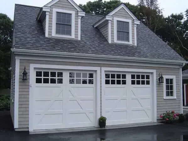 White two-car garage with dormer windows and gray shingled roof, front view of a house.