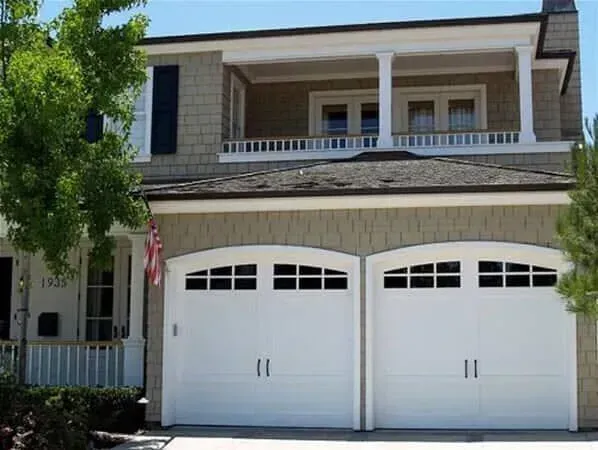 Two-story house with white double garage doors and a balcony under a clear sky