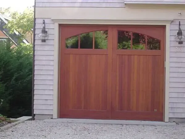 Wooden double garage door with arched windows on a white house exterior