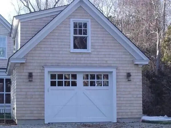 Small beige garage with white door and dormer window, viewed from the driveway.