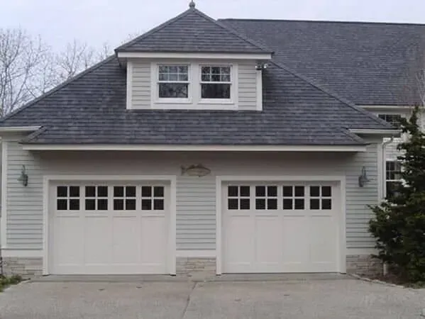 White two-car garage with dormer window and dark shingled roof on a suburban house