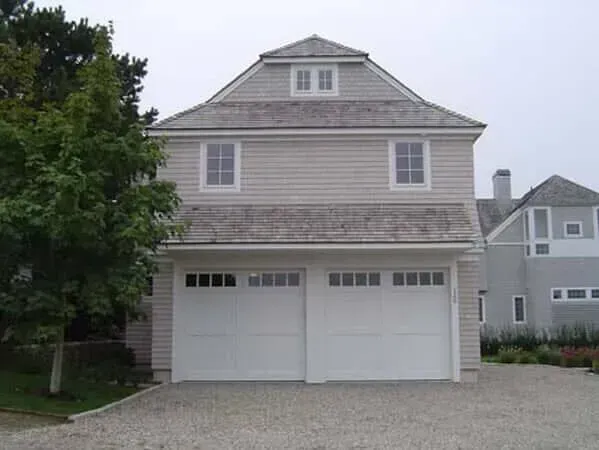 Two-story beige house with white garage doors and a gravel driveway, seen from the front