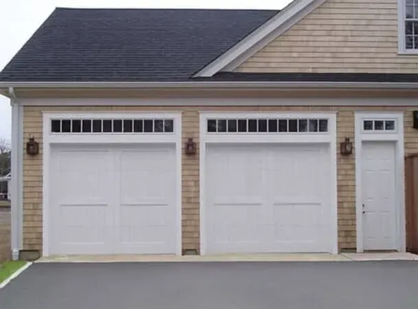 Two white garage doors and a side entry door on a beige suburban house