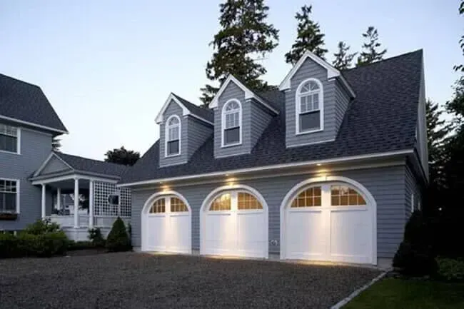 Gray two-story house with three lit garage doors at dusk
