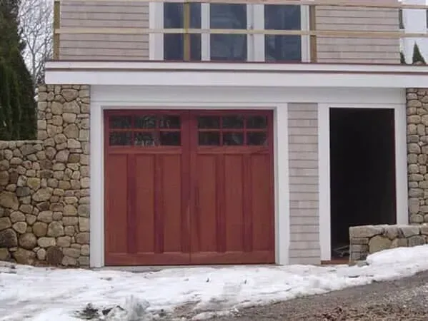 Snowy driveway with a red garage door and open side entrance on a house exterior