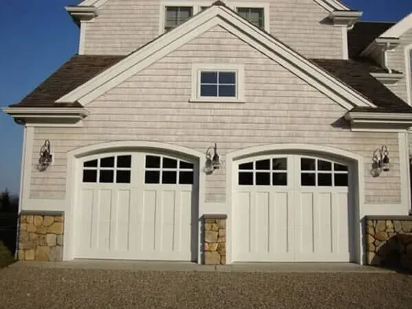 Two beige garage doors with stone accents on a suburban house exterior