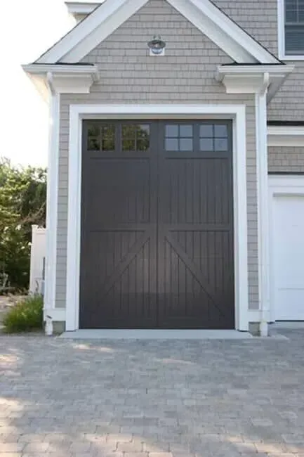Gray garage door with window panes on a house exterior, framed by white trim and stone driveway.