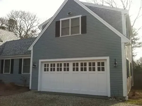 Gray house with white garage door and dark shutters on a cloudy day