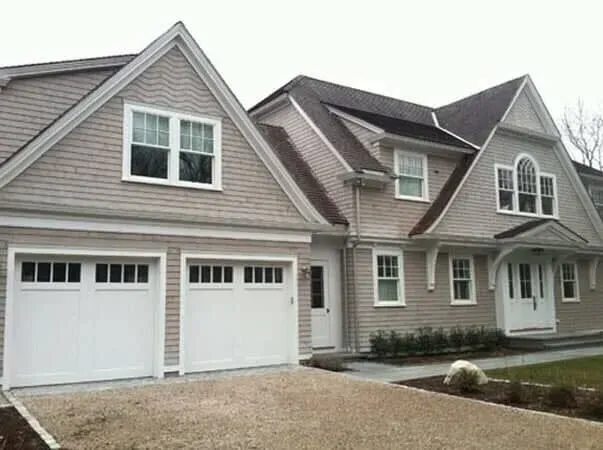 Suburban house exterior with white garage doors, gray siding, and a gravel driveway
