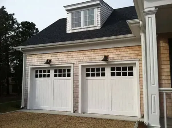 Three-car garage with beige siding, white doors, and a dormer window on top