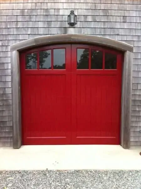 Red garage door with small windows set in a shingled exterior wall.