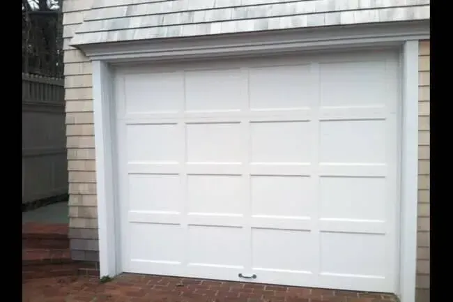 White garage door on a house with light siding and a brick driveway.