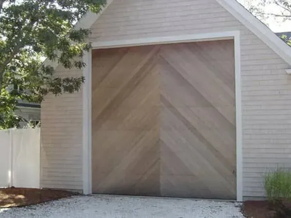Wooden barn-style garage door on a small white outbuilding with a tree and fence nearby