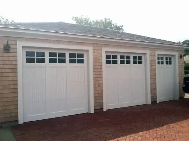 Two white garage doors on a brick driveway attached to a beige house