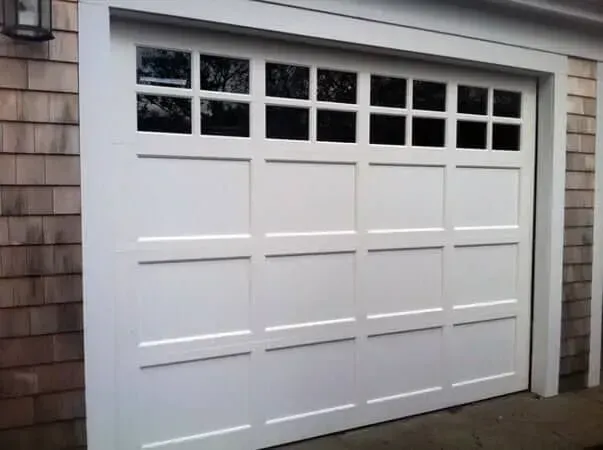 White garage door with small window panes at the top, set in a shingled exterior wall.