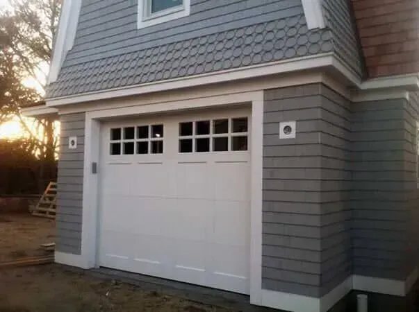 White garage door on gray house exterior with small upper windows at dusk