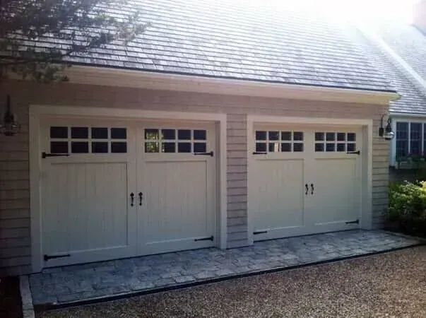 Two white double garage doors on a light gray house exterior with small windows at the top