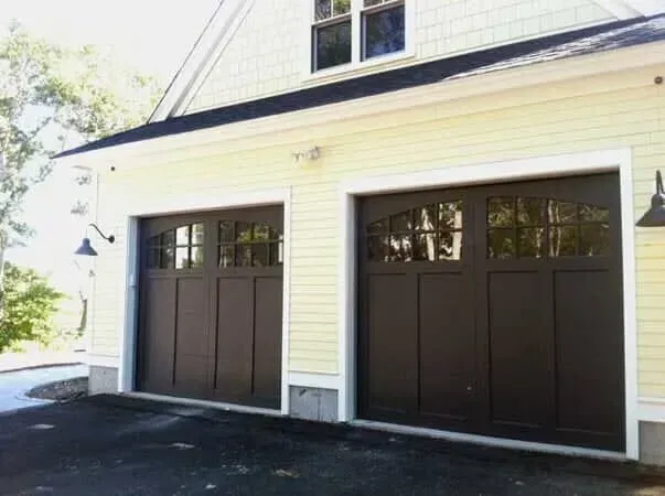 Two dark brown garage doors on a light yellow house exterior