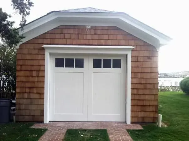 Small white garage with double doors and shingle siding, centered in a grassy yard.