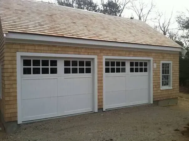 Two white garage doors on a beige house exterior with a small side window