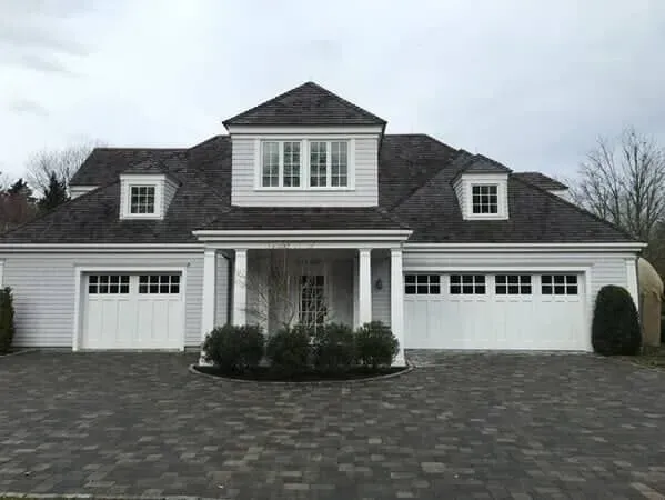 Gray suburban house with white trim, two garages, and a paved driveway under an overcast sky