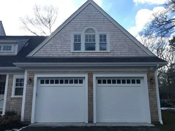 Two-car white garage on a brick house with gray siding and dormer windows
