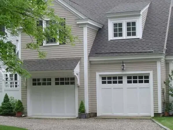 Two white garage doors on a beige house with gray shingles and small window panes.
