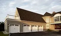 Large beige house with a steep roof and three white garage doors at dusk