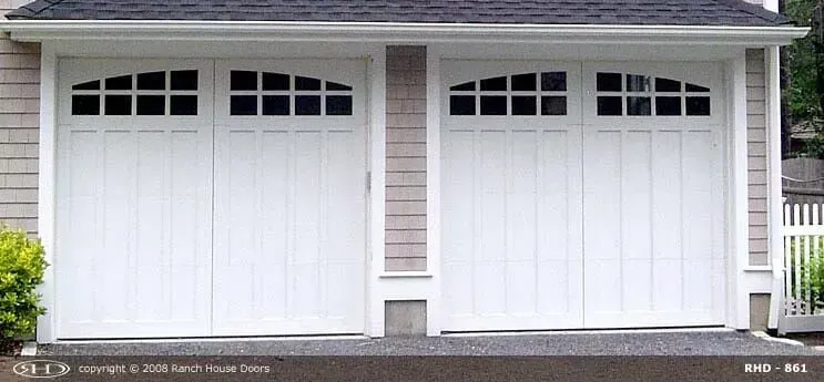 Two white garage doors with arched window panels on a home exterior