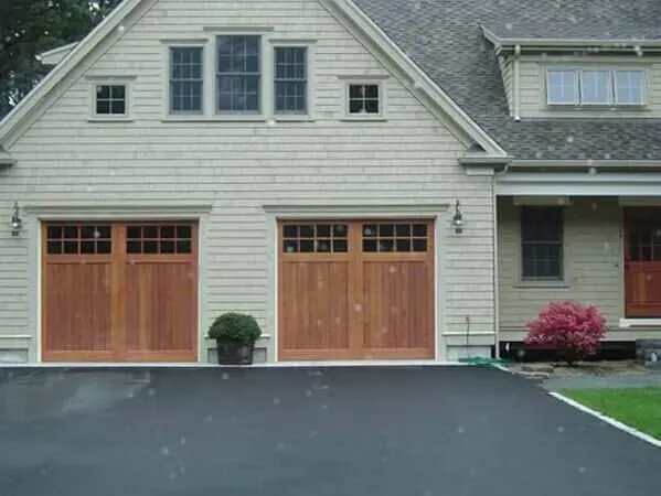 Suburban house with two wooden garage doors, gray siding, and a driveway leading to the entrance