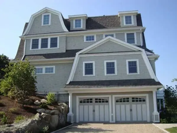 Large gray coastal house with white trim and a double garage under a bright blue sky
