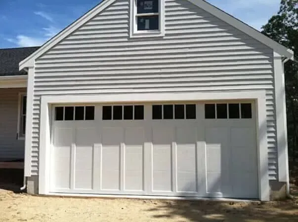 White garage with gray siding and a row of small windows above the door.