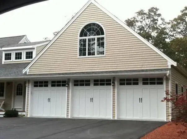 Suburban house with beige siding, three white garage doors, and a large arched window above.