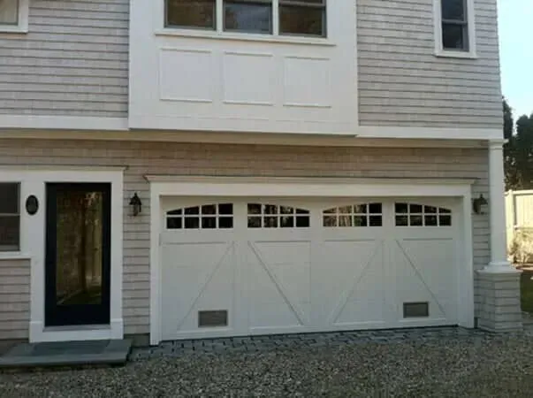 Front view of a two-car garage with white doors on a beige house exterior