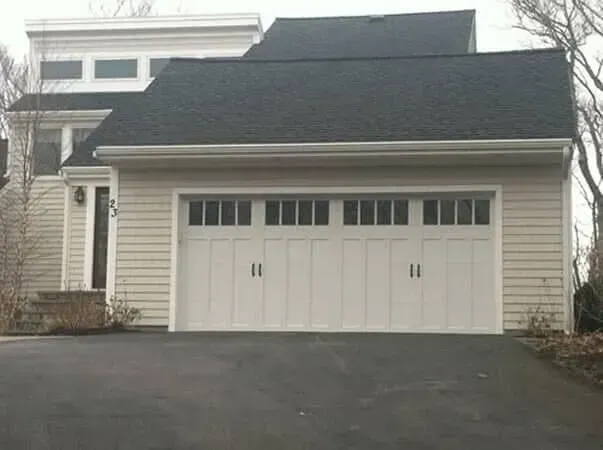 White garage with two doors and dark shingled roof on a sloped driveway