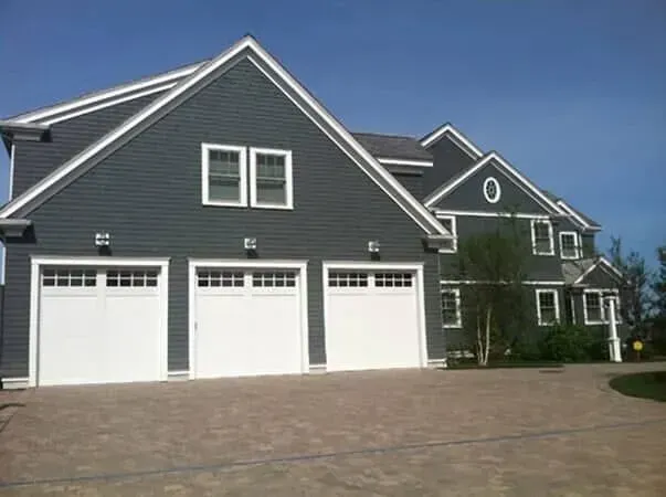 Large dark-gray house with three white garage doors and a paved driveway under a clear blue sky