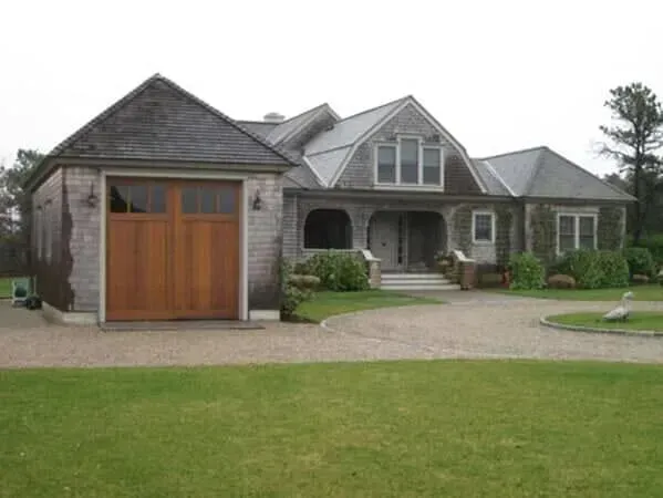 Large stone house with a wooden garage door, arched front porch, and a green lawn.