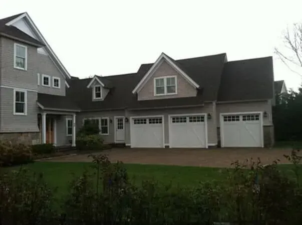 Gray suburban house with three-car garage and front lawn on an overcast day
