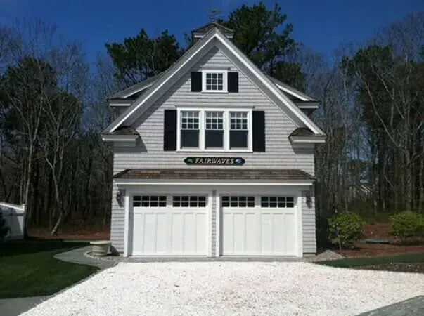 Gray two-story house with white trim, double garage, and gravel driveway in a wooded yard