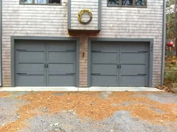 Two gray garage doors on a house with a wreath above them and a gravel driveway in front