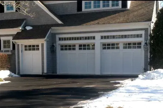 Snow-covered suburban house with a three-car garage and driveway